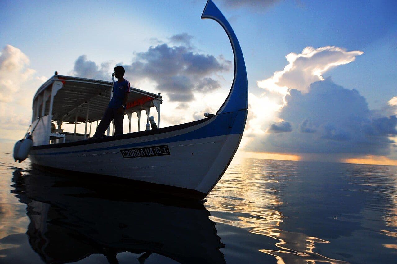 A traditional Maldivian dhoni boat on calm water at sunset